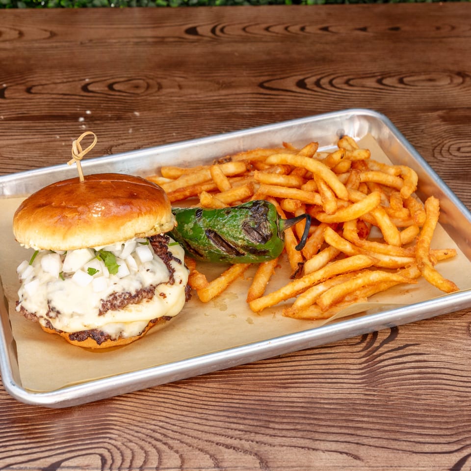 Wagyu Smashburger with melted cheese, diced onions, and a grilled jalapeño, served with fries on a tray.