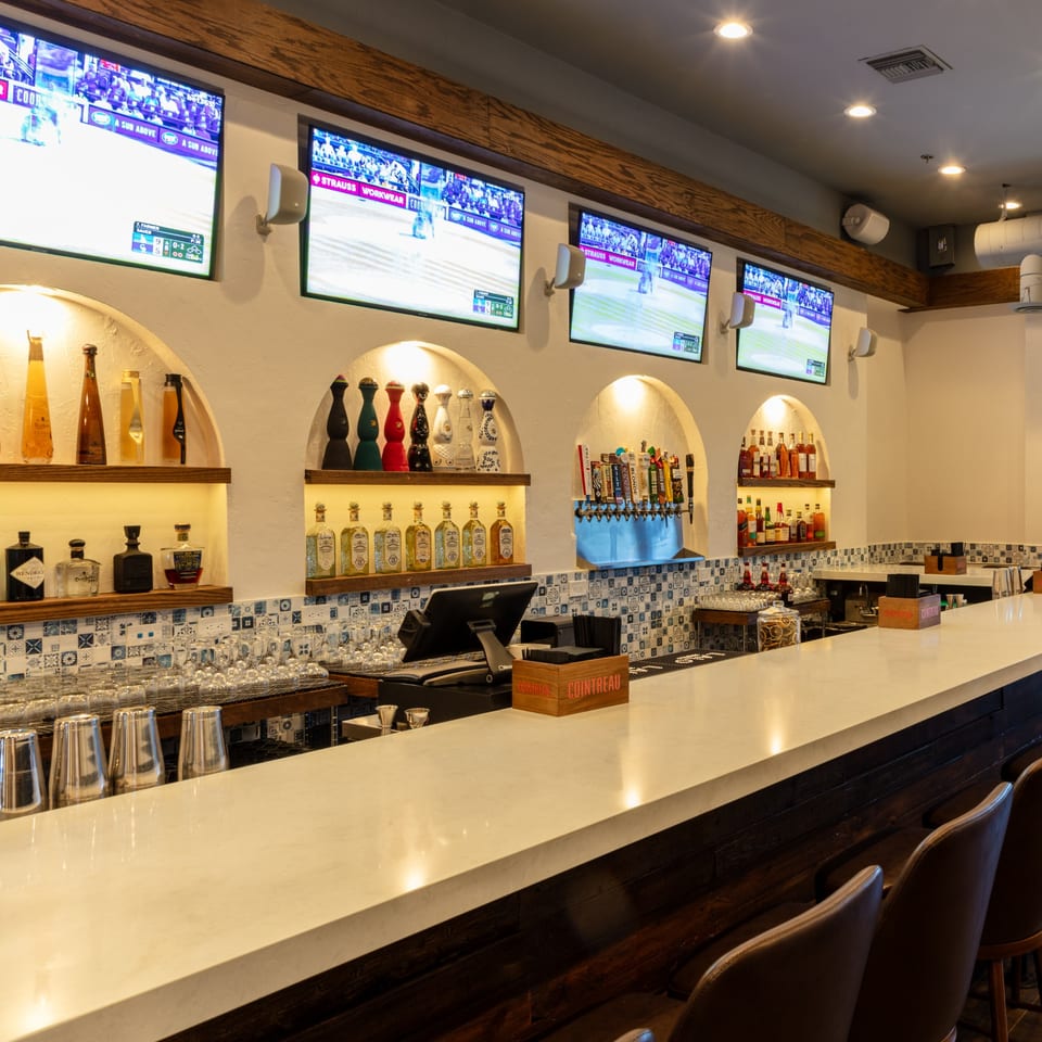 A well-lit bar area with multiple TVs showing sports, liquor bottles on shelves, and beer taps.