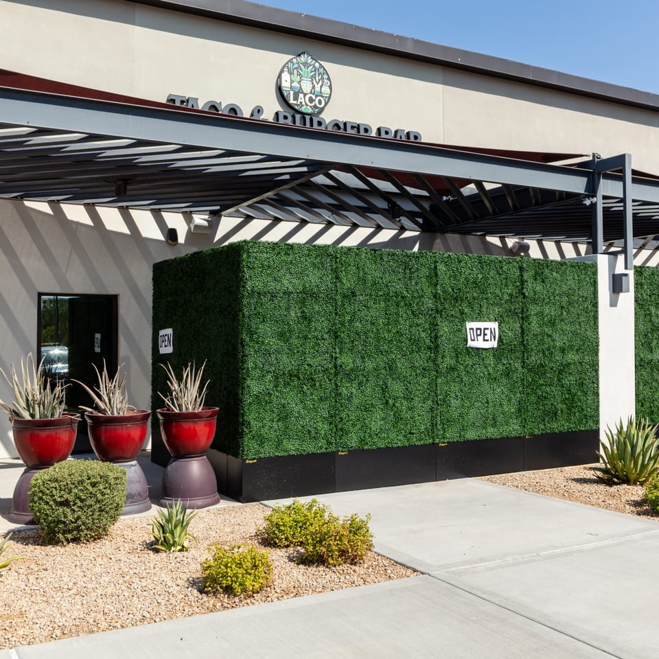 Exterior of Wagyu Smashburgers & Tacos, with a green hedge, red planters, and an "OPEN" sign.